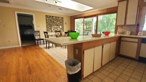 A kitchen with a wooden countertop, a dining area with chairs, and a window with a view of greenery.