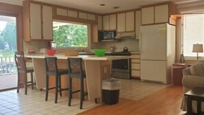A kitchen with wooden cabinets, a refrigerator, a microwave, and a dining area with chairs and a table.