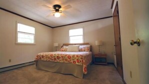 A bedroom with a bed, two windows, a ceiling fan, and a nightstand.