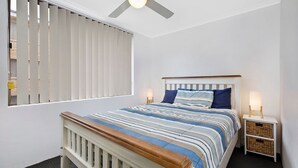 Een slaapkamer met een bed, nachtkastjes, een plafondventilator en een raam met jaloezieën.