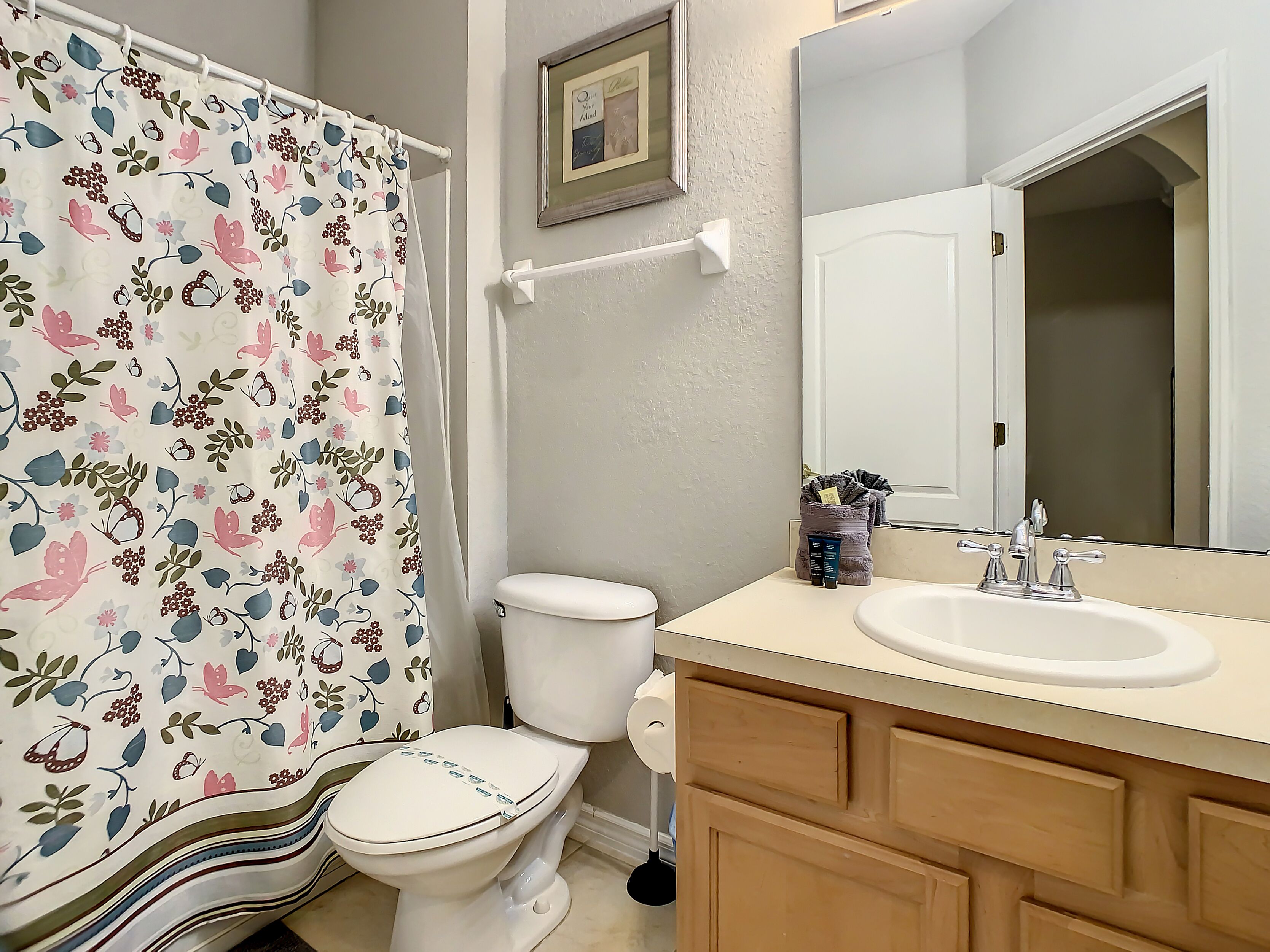 A bathroom with a toilet, a sink, a mirror, and a shower curtain with a floral pattern.