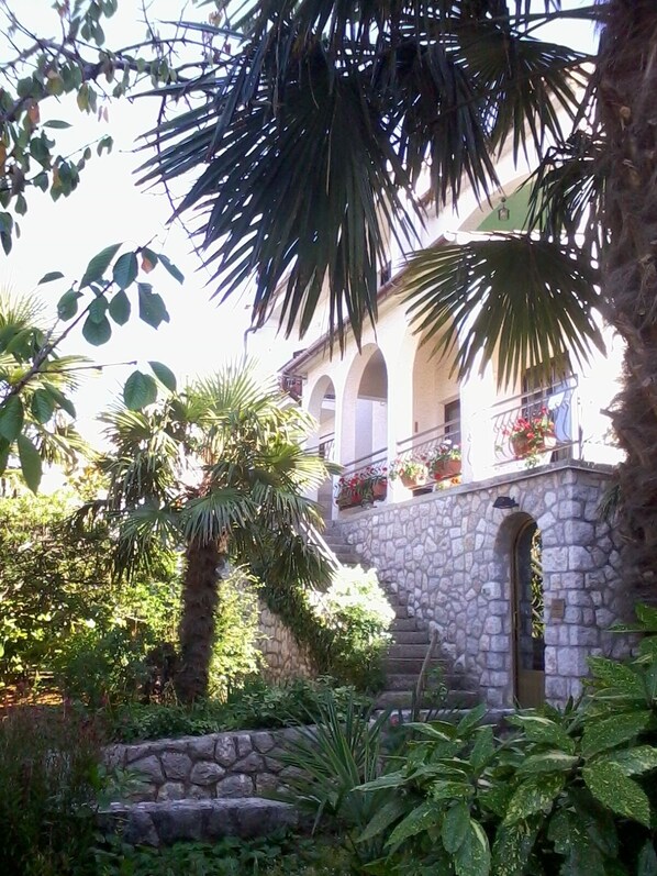 Una escalera de piedra que conduce a un edificio con ventanas de arco y balcones decorados con plantas en macetas.