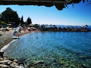 A beach with clear water, umbrellas, and a rocky shoreline. - Apartment NJIVICE *** with Wi-Fi, sea view, air conditioning, 200m from the sea (Njivice)