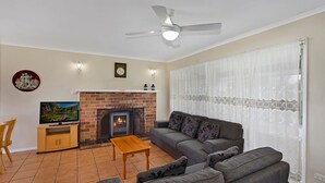 Sala de estar com lareira, sofá, televisão e ventoinha no teto.