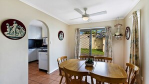 Uma área de refeições com mesa e cadeiras, um ventilador de teto e vista para um quintal através de uma porta de vidro deslizante.