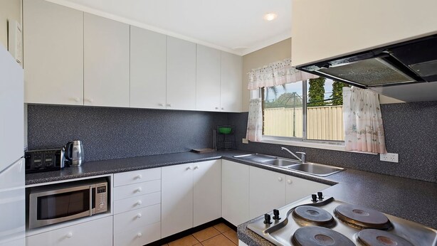 Uma cozinha compacta com armários brancos, micro-ondas, fogão a gás e uma janela com cortinas.
