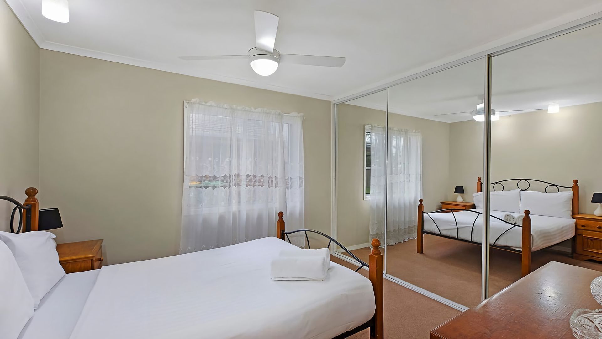 A bedroom with a bed, bedside tables, a mirror, and a ceiling fan.