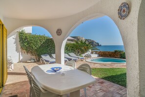 Eine Terrasse im Freien mit Tisch und Stühlen, einem Pool und Blick auf das Meer.