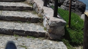 Un escalier en pierre descend vers une zone côtière où un panneau indique « Chemin des amoureux » et « Espace public ».