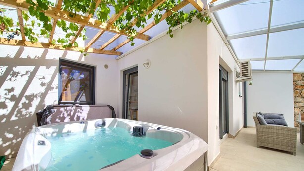 Ein Whirlpool unter einer Pergola mit Blick auf einen Garten und ein Korbstuhl.