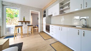 Eine moderne Küche mit weißen Schränken, einer Holz Arbeitsplatte und einem eingebauten Backofen. Zwei Hocker und ein kleiner Esstisch sind vorhanden.