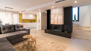 A modern living room with a sofa, two round tables, a fireplace, and a kitchen in the background.