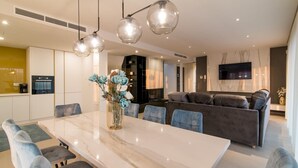 A modern living room with a marble dining table, blue upholstered chairs, a grey sofa, and a vase with flowers.