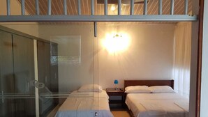 Ein Zimmer mit zwei Betten, einer Glastrennwand, einem Nachttisch mit Lampe und einer Wandleuchte.
