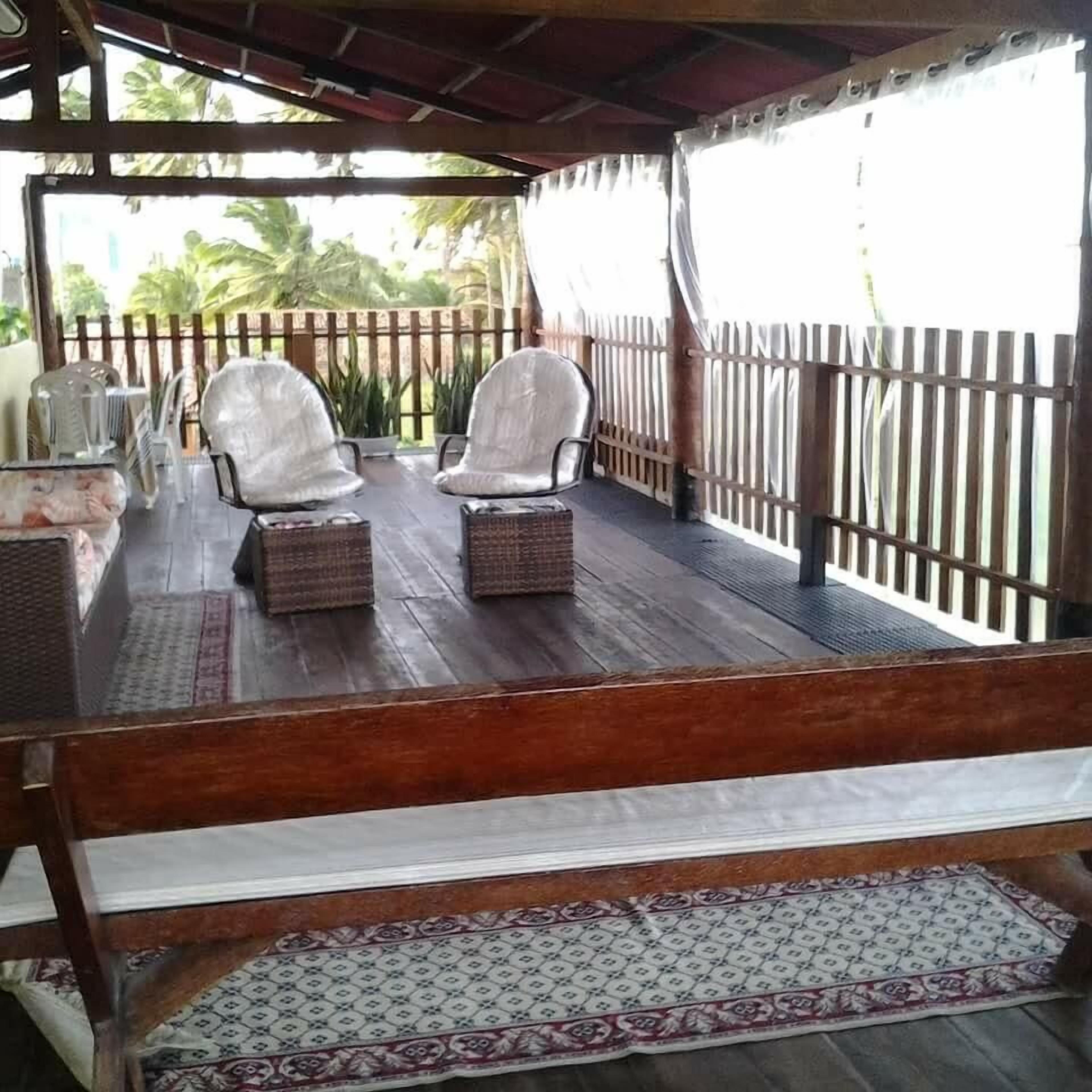 Un área de estar al aire libre techada con dos sillones blancos acolchados y una mesita pequeña, un banco de madera y una alfombra estampada.