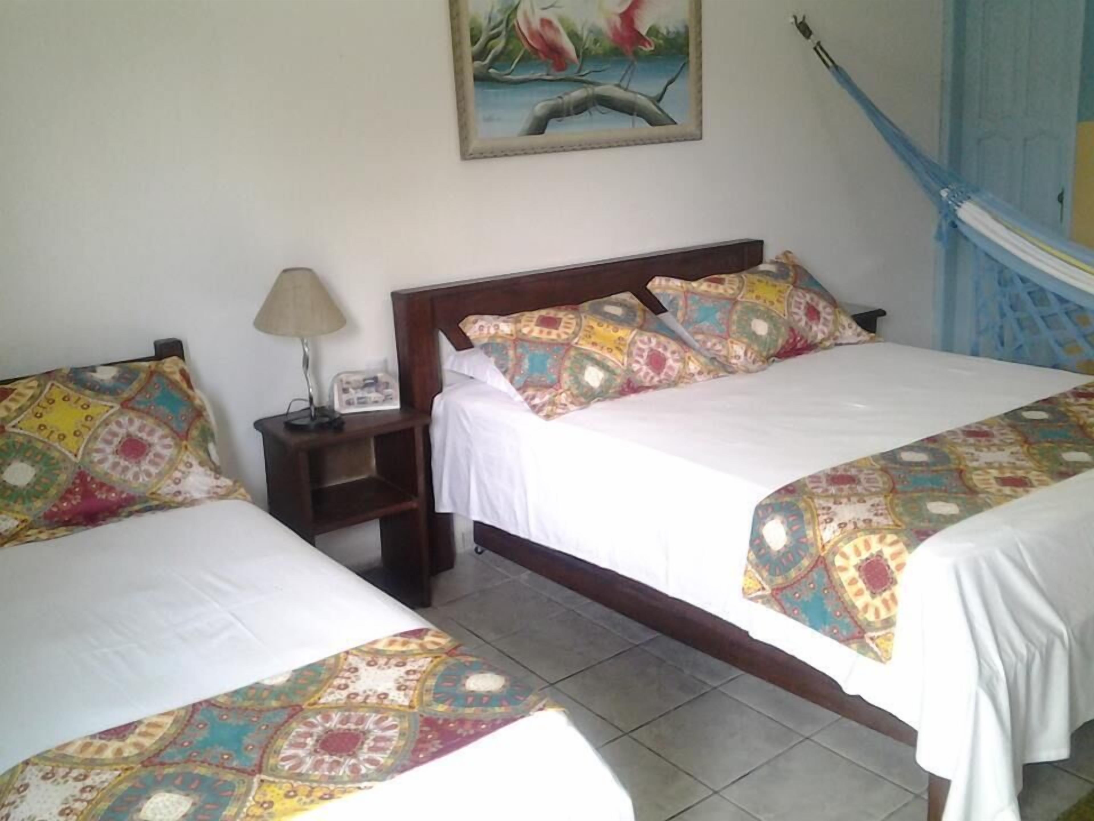 A hotel room with two beds, a nightstand, a lamp, and a painting on the wall.
