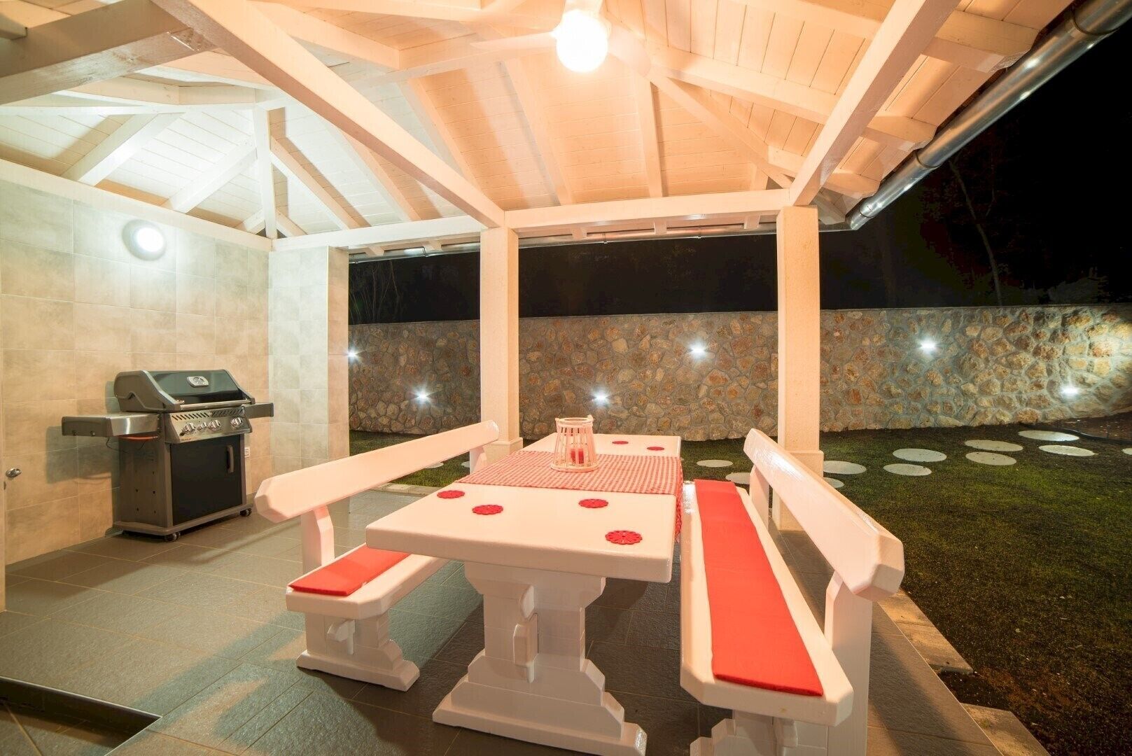 An outdoor patio with a table and benches, a grill, and a stone wall in the background.