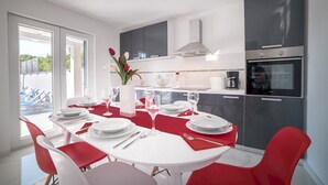 A modern kitchen with a dining area, featuring a white table with red chairs, a vase with flowers, and a view of the outside. - Modern Villa Future**** with an outdoor heated pool in a quiet village on Krk (Klimno)