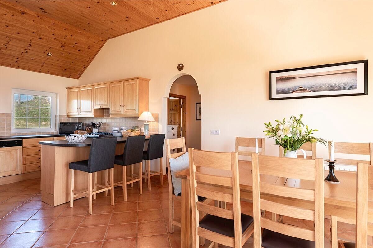 A kitchen with wooden cabinets, a central island with bar stools, and a dining area with wooden chairs.