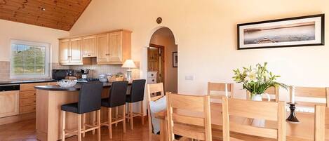 A kitchen with wooden cabinets, a central island with bar stools, and a dining area with wooden chairs.