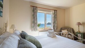 Un dormitorio con una cama grande, vistas al mar a través de una ventana, una silla y una lámpara.