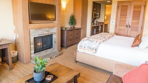 A cozy room with a fireplace, a bed, a TV, and a kitchenette.