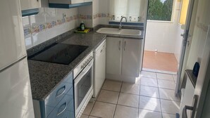 Een keuken met een granieten aanrechtblad, witte kasten, een inbouwoven en een raam met uitzicht op een balkon.
