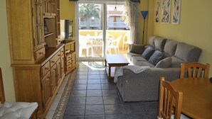 Een woonkamer met een bank, een eettafel en een televisie. Er is een balkon met stoelen en een tafel.