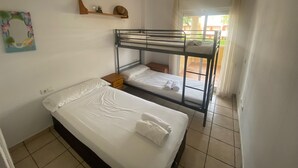 Een slaapzaal met stapelbedden, een enkel bed, een plafondventilator en een raam met gordijnen.