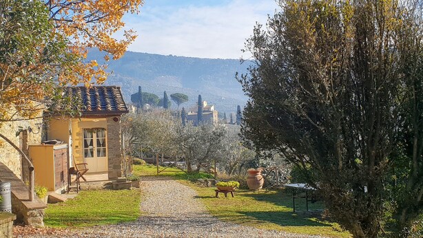 A stone building with a tiled roof, a gravel path, and a view of distant hills. - Romantic cottage on a farm with a view of Cortona (Cortona)