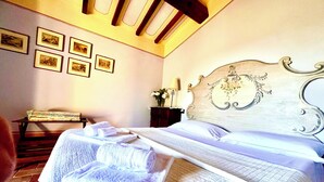 A neatly made bed with folded towels, a headboard with a floral design, and several framed pictures on the wall. - Romantic cottage on a farm with a view of Cortona (Cortona)