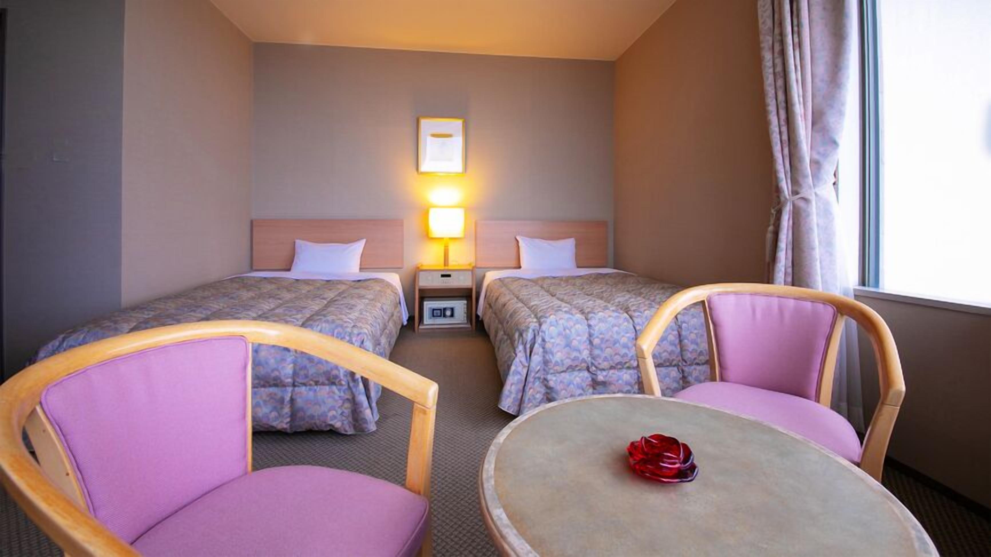 Una habitación de hotel con dos camas, una mesita pequeña y dos sillas.