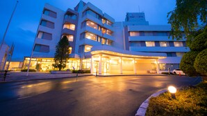 Un hotel de varios pisos con una entrada curva, ventanas iluminadas y un camino de acceso bien cuidado.