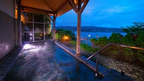 Zona de aguas termales con una terraza de madera y vista al lago al anochecer.