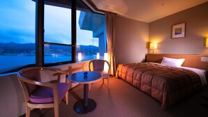 Habitación de hotel con un ventanal grande, una cama, una mesa redonda, dos sillas y vistas a un paisaje urbano.