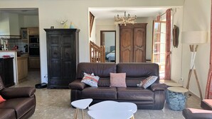 A living room with a brown leather sofa, two white tables, a dark wooden cabinet, and a chandelier. - Spacious property in wooded grounds - not overlooked Monpazier - Private swimming pool (Monpazier)