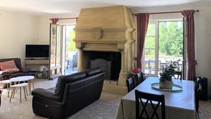 A living room with a fireplace, a sofa, a TV, and a dining area with a table and chairs. - Spacious property in wooded grounds - not overlooked Monpazier - Private swimming pool (Monpazier)