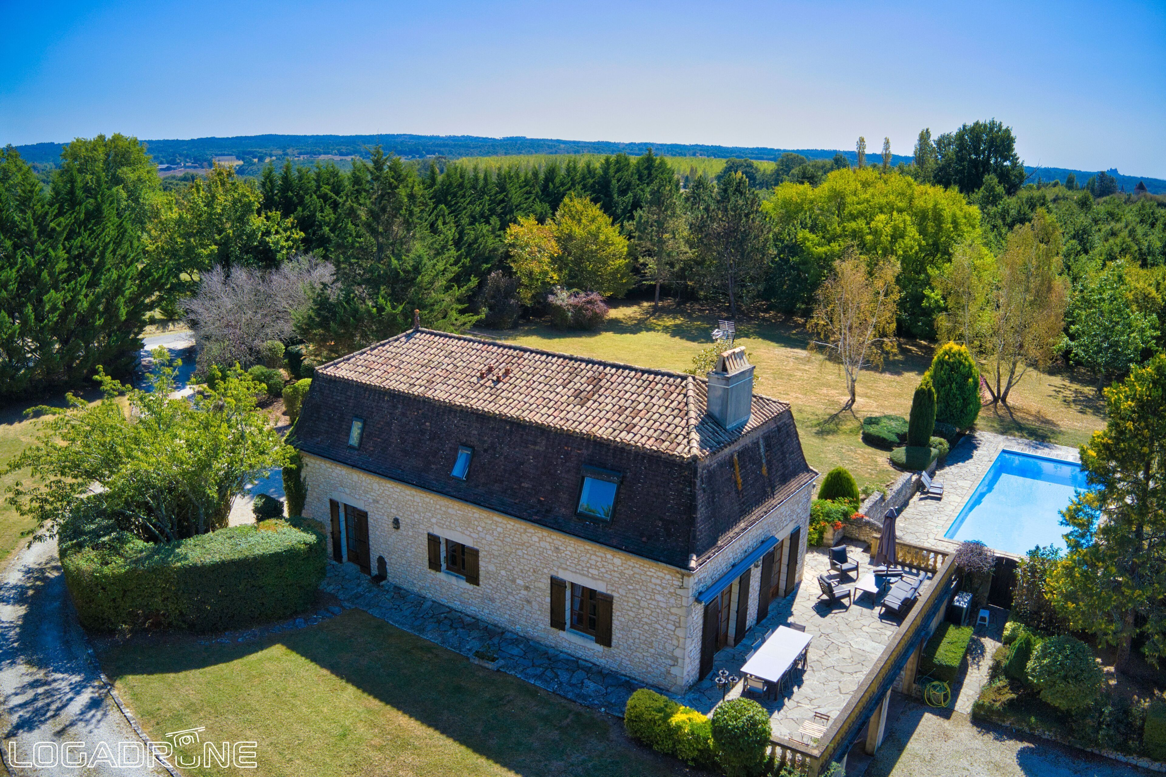 Une maison en pierre avec un toit en tuiles, une piscine et un jardin bien entretenu.