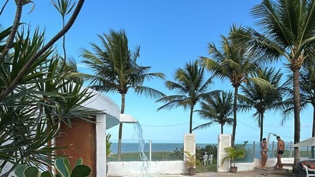 Piscina com vista para o oceano, rodeada por palmeiras e uma pequena cascata.