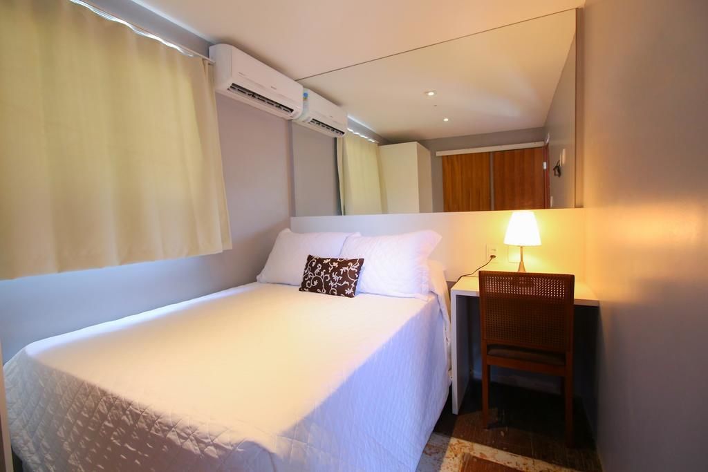 Una habitación de hotel con una cama, una silla, un aire acondicionado y una lámpara.