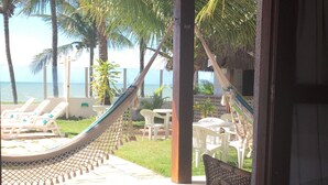 Quarto com uma cama, vista para uma praia com palmeiras e uma rede.