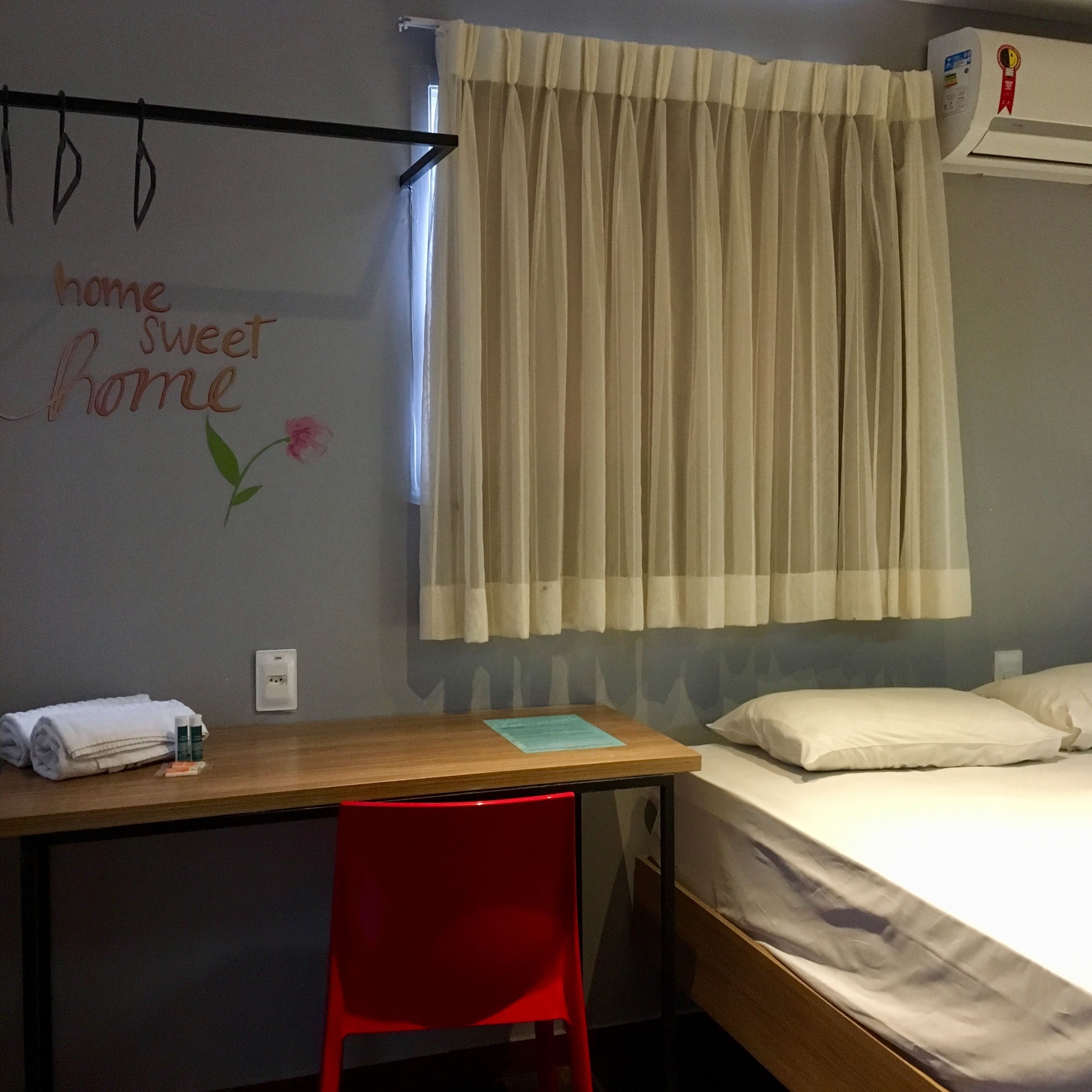 Hotelkamer met een bed, bureau met stoel, luchtverkoeler aan de muur en gordijn.