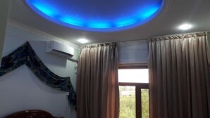 A room with a blue-lit ceiling, a window with curtains, and an air conditioning unit on the wall.