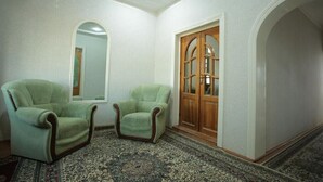 A room with two green armchairs, a wooden door with glass panels, and a patterned carpet.
