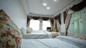 A hotel room with three beds, ornate curtains, and a ceiling with recessed lighting.
