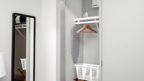 A modern bathroom with a mirror, a white laundry basket, a hanging iron, and a white towel rack. - Studio King Suite w/ Kitchen | 103 (Asheville)