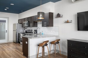 Une cuisine moderne avec des meubles de couleur sombre, un plan de travail en granit et deux tabourets de bar.