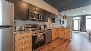 A modern kitchen with stainless steel appliances, wooden cabinets, and a large window providing natural light. - Studio King Suite w/ Kitchen | 103 (Asheville)