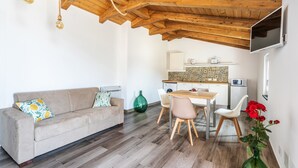 Un accogliente soggiorno con soffitto in legno, un divano con cuscini, un tavolo da pranzo con sedie e una cucina sullo sfondo.