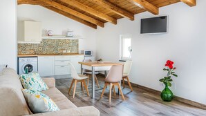 Una cucina moderna con soffitto in legno, un'area pranzo con tavolo e sedie, una lavatrice e un vaso verde con fiori.